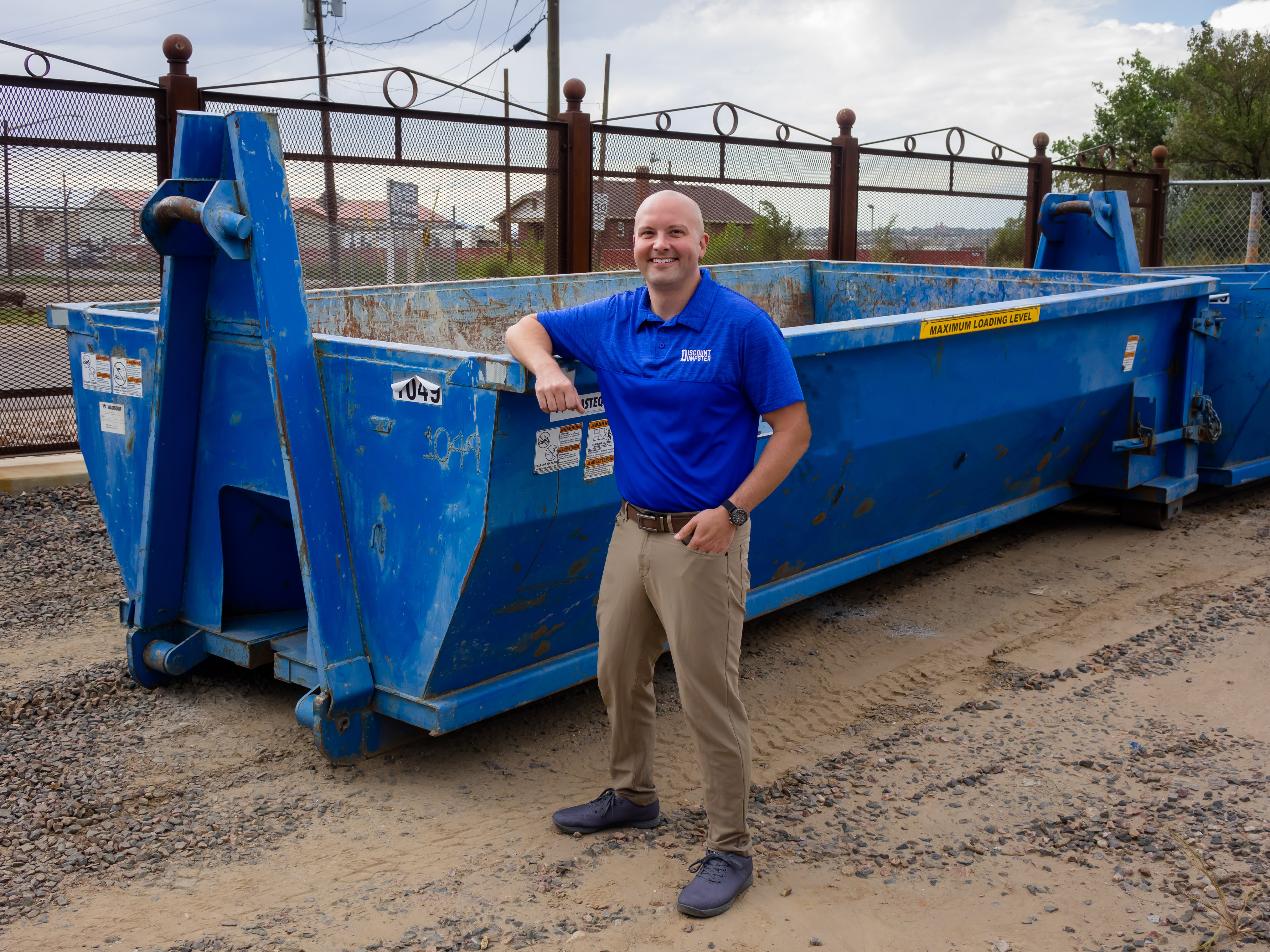 A man leaning on a blue 10 yard dumpster rental