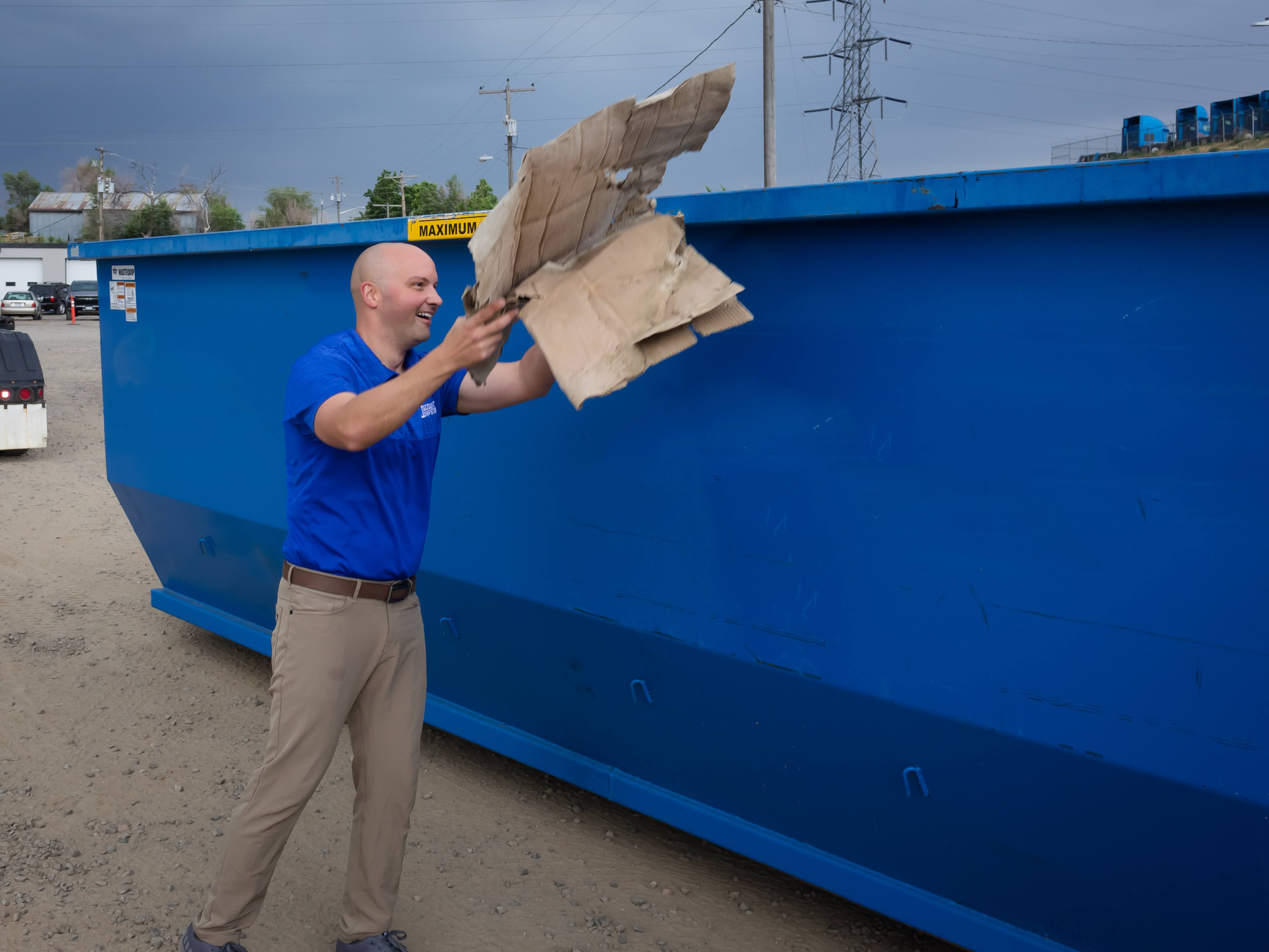 A man tossing contents into a blue 30 yard dumpster rental