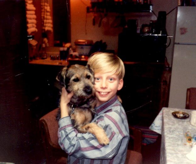 A young boy holding a small dog in a dim lit kitchen.