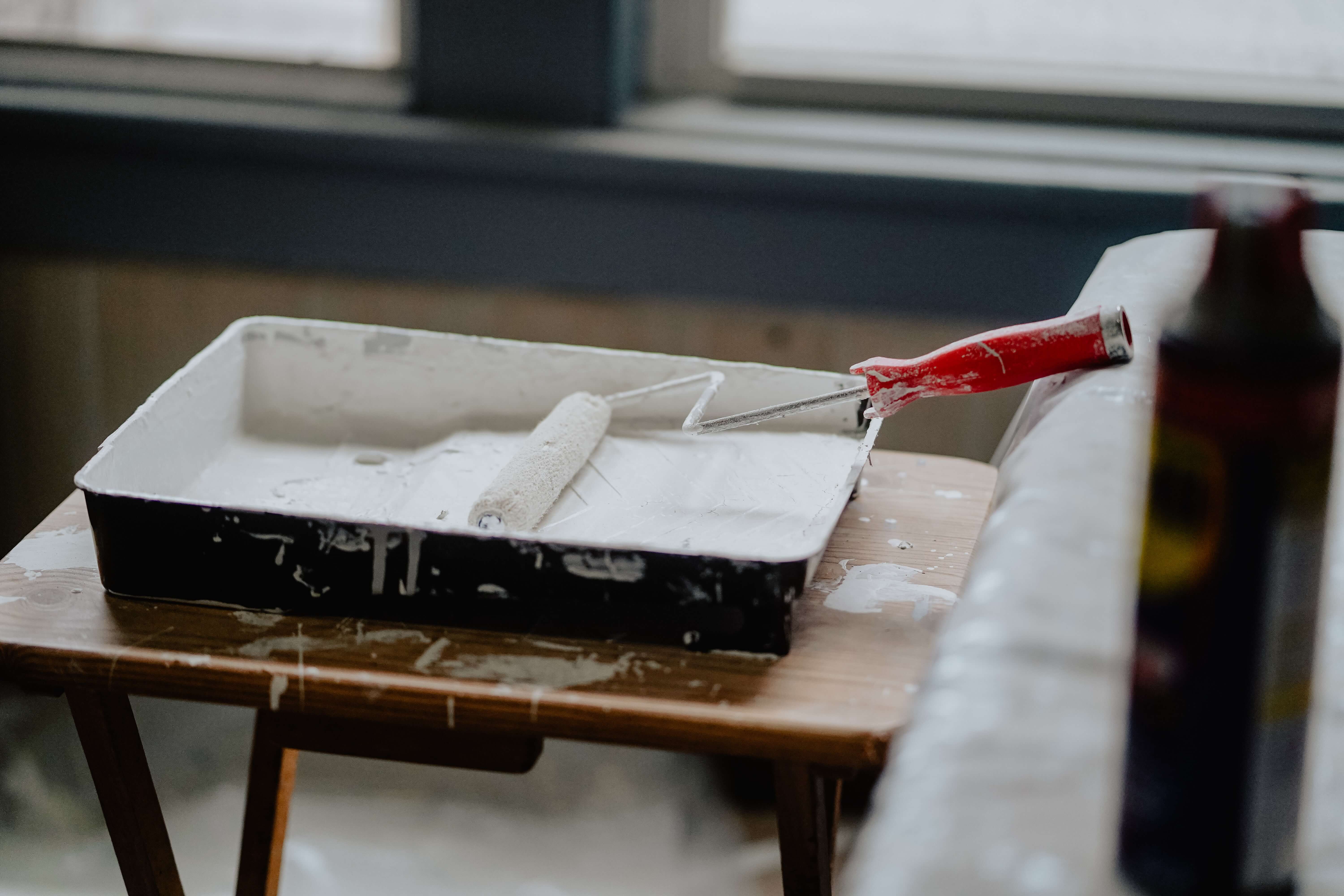 A messy white paint tray with a paint roller on a table.