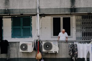 A man outside of his upper level apartment looking down. There are two air conditioning units and clothes drying on a clothesline